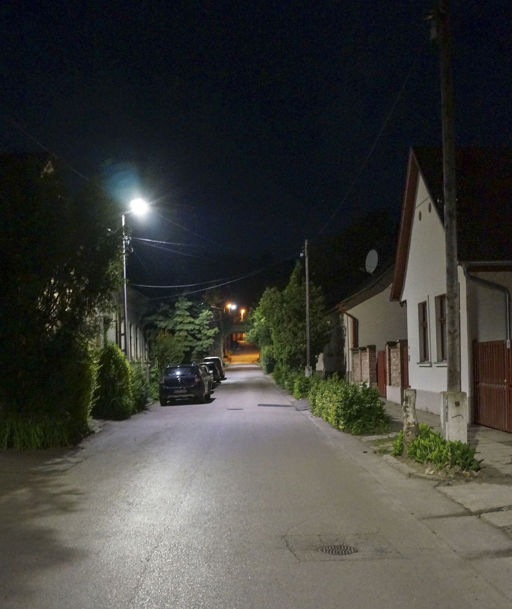 Keskeny nagymarosi utca este, parkoló autókkal, az oszlopon Kombo lámpa.