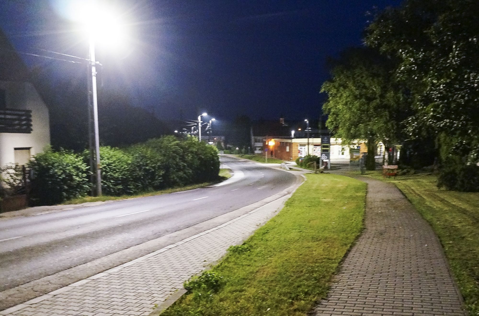 Kanyarodó főút járdával és füves sávval este, az oszlopokon Kombo lámpák.